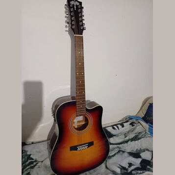 Akustická kytara s cutawayem v přechodovém žlutě-černém provedení (sunburst). Na hlavě hmatníku je viditelné bílé logo ve tvaru ptáka. Hmatník obsahu…