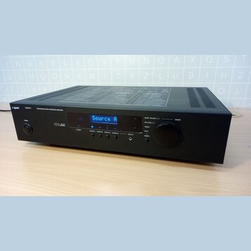 Černý digitální zesilovač s nápisem Apart CONCEPT 1 PROFESSIONAL DIGITAL CONTROLLED AMPLIFIER. Na předním panelu je modrý displej s textem Source A,…