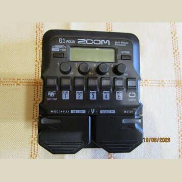 Černý multi-efektový procesor s nápisy G1 FOUR, ZOOM a Multi-Effects Processor. Zařízení má malý displej, čtyři otočné ovladače s popisky Lo, Mid, Hi…