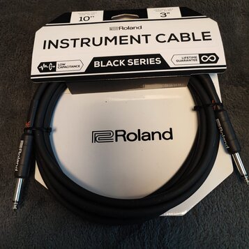 Černý instrumentální kabel s konektory typu jack, sbalený do kruhu. Na obalové kartonové podložce je nápis INSTRUMENT CABLE, BLACK SERIES a logo Rola…