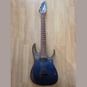 Elektrická kytara s modrým přechodovým lakem a viditnou strukturou dřeva na hranách. Na hlavě hmatníku je bílý nápis Ibanez. Nástroj má dva humbucker…