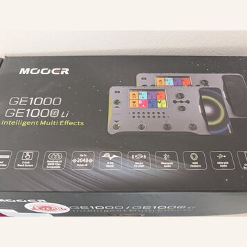 Fotografie znázorňuje krabici od efektového pedálu s nápisy MOOER, GE1000 a GE1000 Li Intelligent Multi-Effects. Na krabici je zobrazen šedý přístroj…