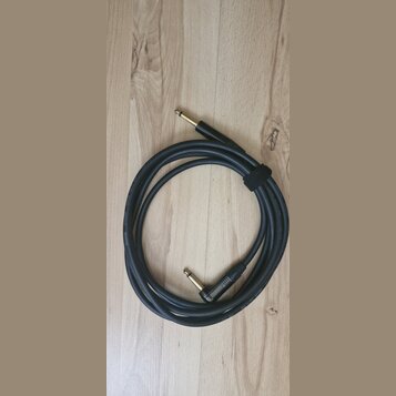 Černý instrumentální kabel s pozlacenými konektory typu jack. Na povrchu kabelu je bílý nápis GUITAR INSTRUMENT CABLE. Kabel je svázaný černým suchým…