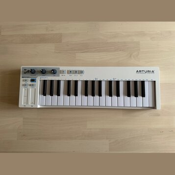 Bílá klaviatura s 32 klávesami. Na pravé straně je nápis ARTURIA a pod ním slogan YOUR EXPERIENCE YOUR SOUND, vlevo je označení KEYSTEP. Horní panel…