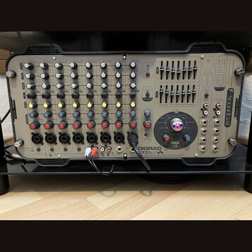 Šedý mixážní pult v černém transportním kufru. Na pravé straně je svisle napsáno logo Soundcraft a v dolní části nápisy GIGRAC 1000sc, GIG a combined…