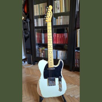 Elektrická kytara typu Telecaster v krémové barvě se světlým hnedem dřevěného krku a hmatníkem. Na hlavě je viditelné logo "Telecaster". Tělo vykazuj…
