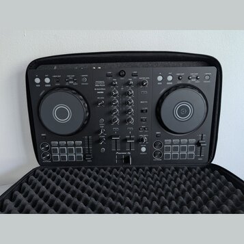 Černý DJ kontrolér Pioneer DJ model DDJ-FLX4 umístěný v černé polstrované přepravní brašně. Na přístroji jsou viditelné nápisy rekordbox a serato. Po…