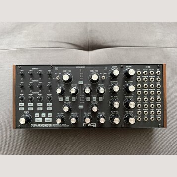 Stříbrný semi-modulární analogový syntetizátor s dřevěnou bočními stěnami. Na předním panelu je vlevo dole nápis SUBHARMONICON | SEMI-MODULAR ANALOG…