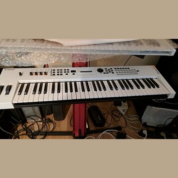 Bílá klávesová syntezátor s černými klávesami umístěná na červeném stojanu. Na levé straně je nápis YAMAHA a v pravém horním rohu označení MX61. Horn…