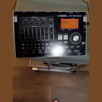 Černý digitální nahrávací zařízení s nápisem BOSS DIGITAL RECORDER BR-800. Přístroj obsahuje displej, několik posuvníků track mixeru, ovládací knoflí…