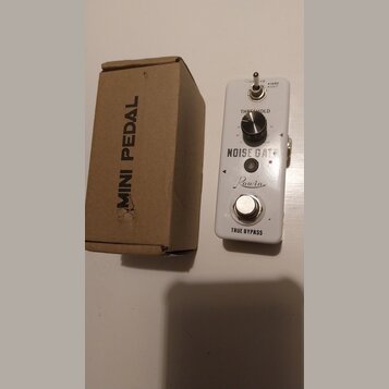 Bílý efekt pedál s nápisy NOISE GATE, Rowin a TRUE BYPASS. Obsahuje jeden ovládací knoflík s popiskem THRESHOLD a přepínač s označením HARD / SOFT. V…