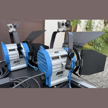 Dvě stříbrno-modré studiové lampy s černými klapkami. Na obou je vidět nápis ARRI 650. Pravá lampa má štítek s textem ARRI, ARRI 650 a číslem 32 7940…