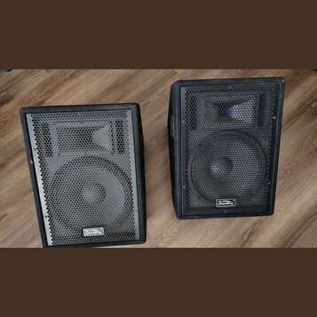 Dva černé reproduktory v hranatých bednách s kovovými ochrannými mřížkami. Na spodní části mřížek je umístěno logo s nápisem Soundking. Povrch beden…