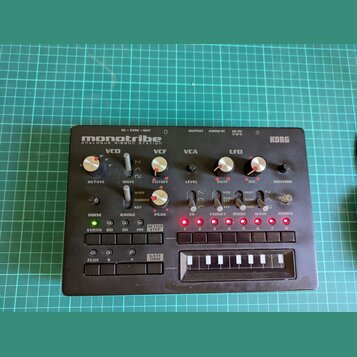 Černý kompaktní syntetizátor s nápisy monotribe ANALOGUE RIBBON STATION a KORG. Přístroj obsahuje několik otočných potenciometrů, přepínačů a řadu tl…