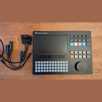 Černý sampler Polyend Tracker s displejem, mřížkou bílých podsvícených polí a ovládacím knoflíkem. Na horní hraně je bílý nápis Polyend Tracker s log…