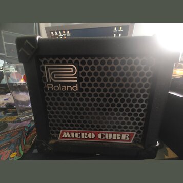 Černý kytarový kombo zesilovač s kovovou mřížkou reproduktoru. Na přední straně je umístěno logo Roland a nápis MICRO CUBE v červeném rámečku. Povrch…