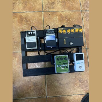 Sada efektových pedálů na černém pedalboardu. Na horní řadě jsou pedály s nápisy Noise Suppressor NS-2, Driver HG-1X a Markbass COMPRESSORE s nápisem…