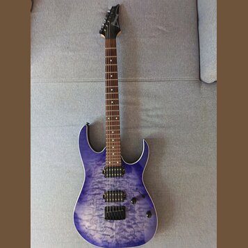 Elektrická kytara s modrým průsvitným povrchem s výraznou strukturou dřeva. Na hlavě hmatníku je viditelné logo Ibanez. Nástroj má dva humbuckery, je…