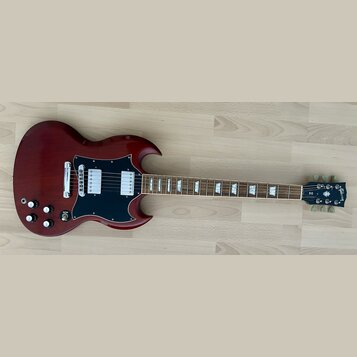 Tmavě červená elektrická kytara s černým pickguardem a dvěma humbuckery. Na hlavě hmatníku je bílý nápis Gibson a pod ním označení SG. Nástroj vykazu…