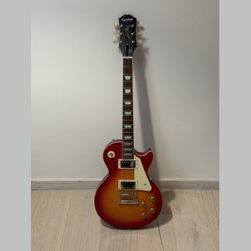 Elektrická kytara s trupem v červeně-žlutém sunburst provedení a bílým pickguardem. Na hlavě hmatníku je bílý nápis Epiphone a pod ním kurzivou Les P…