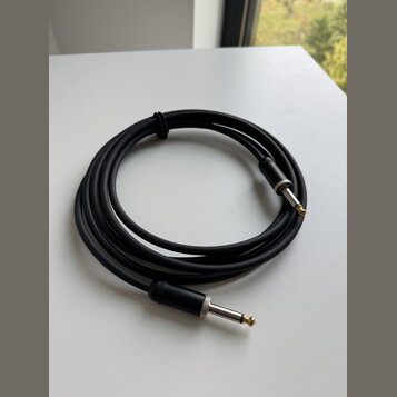 Černý instrumentální kabel s konektory typu jack. Konektory mají stříbrné kovové části a zlaté hroty. Kabel je svinutý do kruhu a upevněný černým sta…