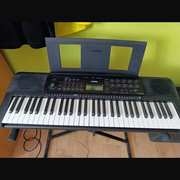 Černý digitální klavír s bílými a černými klávesami, umístěný na černém stojanu. Na horním panelu a na notovém pultu je bílé logo YAMAHA. V pravé čás…