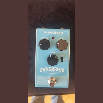 Modře barevný efekt pedál s nápisy tc electronic, SKYSURFER a REVERB. Na horní straně jsou tři černé ovládací knoflíky s popisky REVERB, MIX a TONE,…