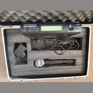 V hliníkovém kufru s pěnovou výplní je umístěn bezdrátový mikrofonní systém. Černý přijímač nese nápisy AWM200 WIRELESS MICROPHONE SYSTEM, UHF a logo…
