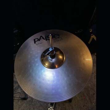 Kruhový činel z lehce žlutého kovu s koncentrickými rýhami na povrchu. Na povrchu je černý nápis Paiste 2002 a pod ním text 16" HI-HAT TOP. Činel je…