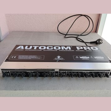 Stříbro-černý rackový procesor s nápisem AUTOCOM PRO AUDIO INTERACTIVE DYNAMICS PROCESSOR MODEL MDX 1400. Na horním panelu je logo BEHRINGER, značka…