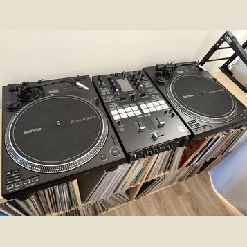 Sada černého DJského vybavení skládající se ze dvou kontrolérů a jednoho mixéru. Na obou kontrolérech jsou vidět nápisy serato a rekordbox. Středový…