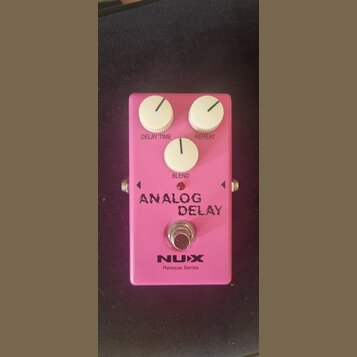 Růžový efekt pedál Analog Delay s třemi bílými oválnými knoflíky označenými jako DELAY TIME, REPEAT a BLEND. Na spodní části je nápis ANALOG DELAY, l…