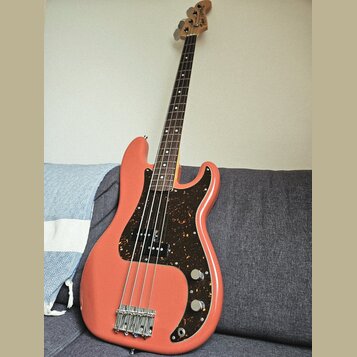 Elektrická basová kytara s růžovým trupem a hnědým hmatníkem. Nástroj má tmavě hnědý pickguard s leopardím vzorem a čtyři struny. Na hlavě krku je vi…