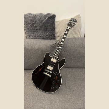 Černá polodublová elektrická kytara s bílým lemováním a černým pickguardem. Na hlavě hmatníku je viditelné logo Gibson. Nástroj má dva humbuckery, čt…