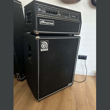 Černý basový kombozesilovač složený z hlavního zesilovače a reproduktorové skříně. Na horním modulu je nápis SVT-450 a logo Ampeg, na spodní skříně j…