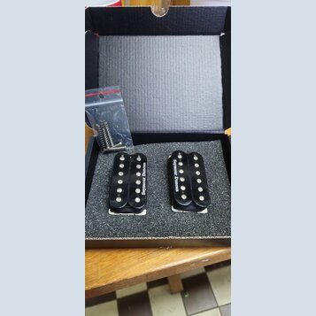 V černé krabičce s pěnovou výplní jsou dva černé humbuckery. Oba mají bílý nápis Seymour Duncan. Vedle nich je v průhledném plastovém sáčku sada mont…