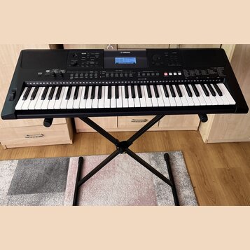 Černý digitální klavír značky YAMAHA, model PSR-E463, umístěný na černém X-stojaně. Nástroj má bílé a černé klávesy a horní panel s displejem, tlačít…