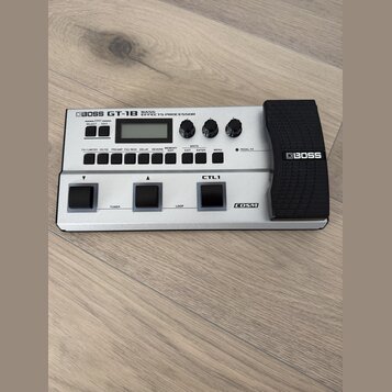 Stříbrný basový efektový procesor značky BOSS, model GT-1B BASS EFFECTS PROCESSOR. Zařízení má digitální displej, několik ovládacích knoflíků a čtyři…
