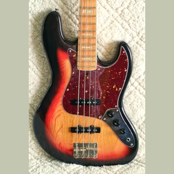 Čtyřstrunná elektrická basová kytara s korpusem v červeno-žlutém sunburst provedení a viditnou strukturou dřeva. Nástroj má tmavě červený pickguard s…