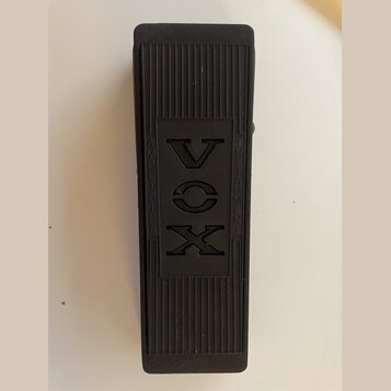 Černý obdélníkový pedál s povrchem z rýhované gumy. Uprostřed je vyryto logo VOX a nápisy AMPLIFIER a INSTRUMENTS. Povrch vykazuje mírné známky opotř…