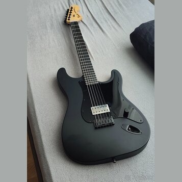 Černá elektrická kytara s matným povrchem a černým pickguardem. Na hlavě hmatníku je viditelné logo Fender. Nástroj má jeden humbucker v pozici kobyl…