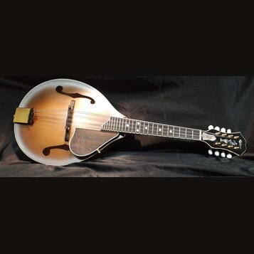 Mandolina s hruškovitým korpusem v přechodovém žlutohnědém odstínu s bílým okrajem. Na hlavě je vidět nápis "Gibson" a dekorativní ornament. Hmatník…