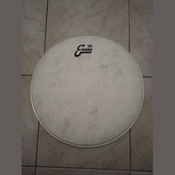 Bílá kruhová bubenová kože v kovovém obruči. Na pravé straně je černé logo s nápisy „Evans“ a „'56“ a menším textem „CRAFTED IN USA“. Povrch kože vyk…