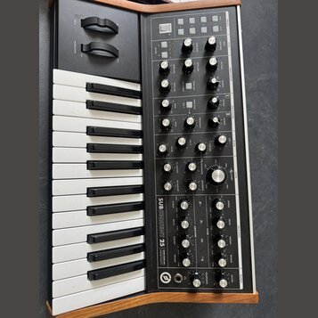 Černý analogový syntetizátor s klaviaturou a dřevěnými bočními panely. Na předním panelu je v bílém nápisu model SUBSEQUENT 25 a logo Moog. Přístroj…