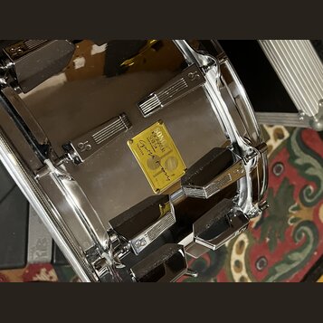 Detailní pohled na chromovaný obrub bubnu s několika kovovými mechanismy. Uprostřed je žlutý štítek s nápisy SONOR SIGNATURE SERIES 50, Made in Germa…