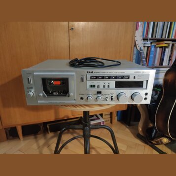 Stříbrný kazetový přehrávač s nápisem AKAI STEREO CASSETTE DECK Model GX-F80. Přístroj obsahuje vložení kazety, ovládací tlačítka a dva velké bílé ov…