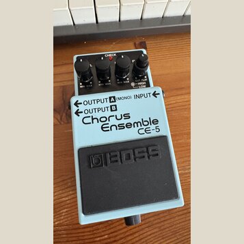 Světle modrý efekt pedál značky BOSS, model Chorus Ensemble CE-5. Na horní části jsou čtyři černé ovládací knoflíky s popisky MIN MAX a CUT FLAT HIGH…