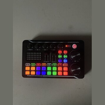 Černý zvukový mixér s řadou barevných tlačítek a ovládacích prvků. Na horní části jsou čtyři černé otočné knoflíky s popisky -TREBLE+, -MID +, -BASS…