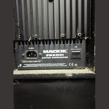 Detail zadní strany černého aktivního subwooferu. Na přístrojovém panelu je nápis MACKIE SWA1501 ACTIVE SUBWOOFER, napájecí konektor označený jako PO…
