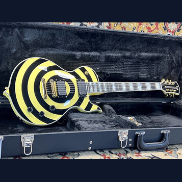 Elektrická kytara s jednovýřezem v tvrdém kufru. Tělo má výrazný žlutý a černý kruhový vzor, zlatý hardware a dva humbuckery. Na hlavě hmatníku je vi…